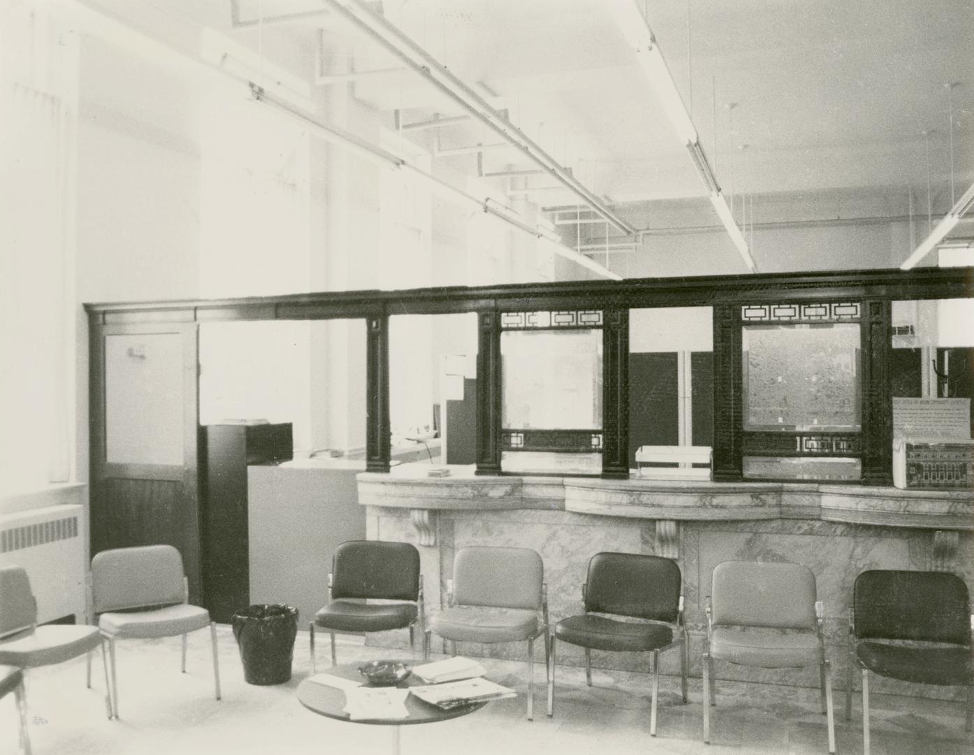 Picture of interior of postal station showing marble counters and a line of chairs. 
