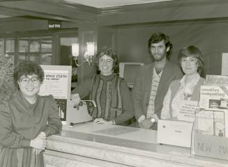 Picture of four staff members standing at a desk in a library. 