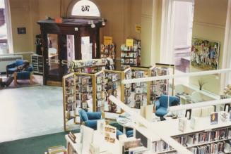 Picture of interior of library showing shelves and seating area and corner entrance door. 