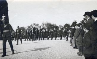 A photograph of a military parade, with dozens of men wearing uniforms and pith helmets marchin ...