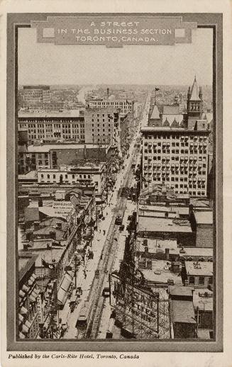  Black and white, aerial shot of a long street with streetcars surrounded by tall buildings.