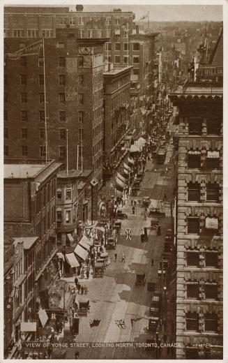 Black and white aerial photograph of skyscrapers on both sides of a busy street decorated with  ...