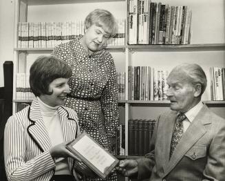 Picture of man presenting a plaque to woman and another woman looking on. 