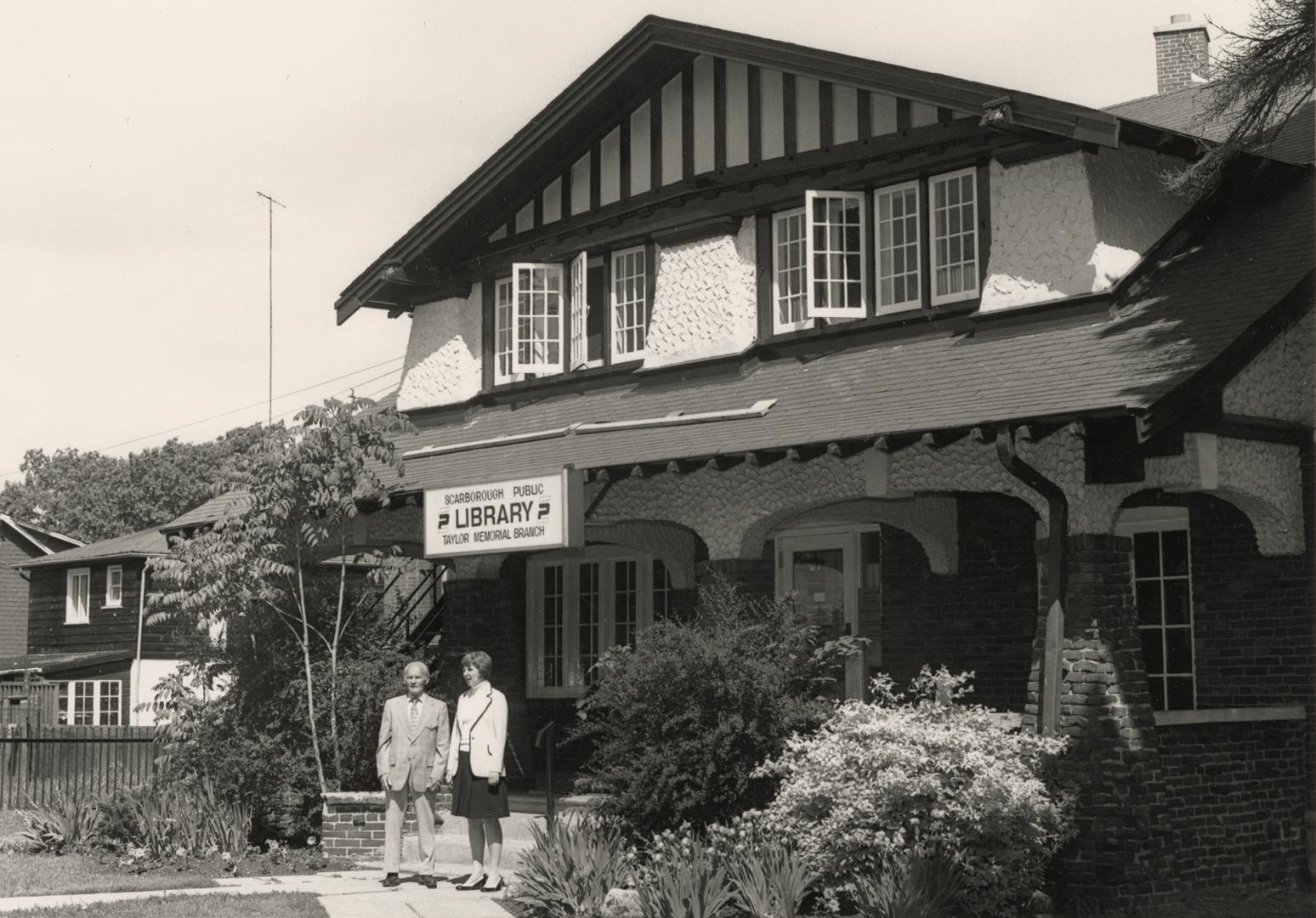 Picture of two people standing outside arts and craft style house used as a library. 