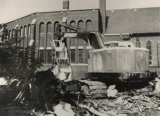 Picture of buldozer demolishing building with other buildings in background. 