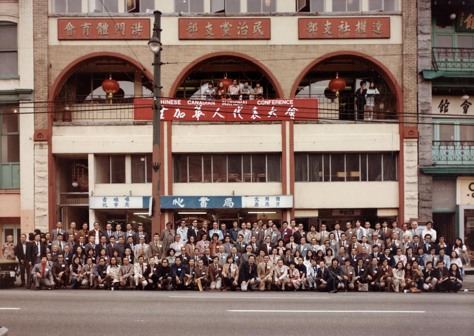 Photograph of a large group of people posed in front of a building.