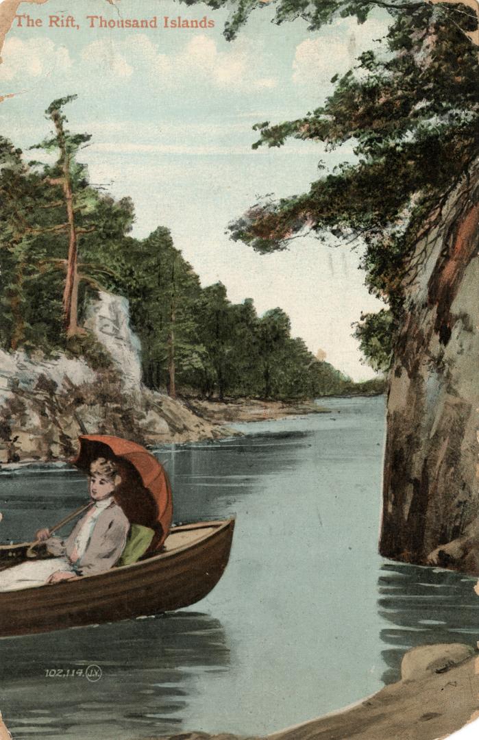 A woman sitting in a row boat on a narrow body of water surrounded by trees.