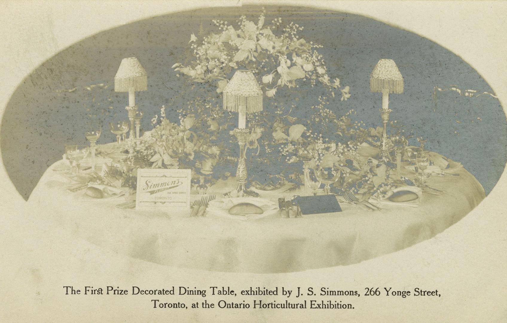 Black and white photo postcard depicting a decorated dining table, adorned with tableware, cand ...