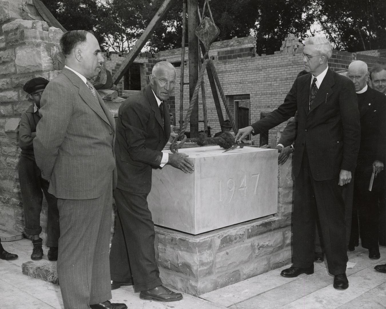 Picture of a group of people gathered at a building cornerstone saying 1947. 