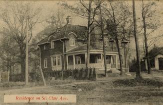 Black and white photograph of a large, two story house with a circular veranda.