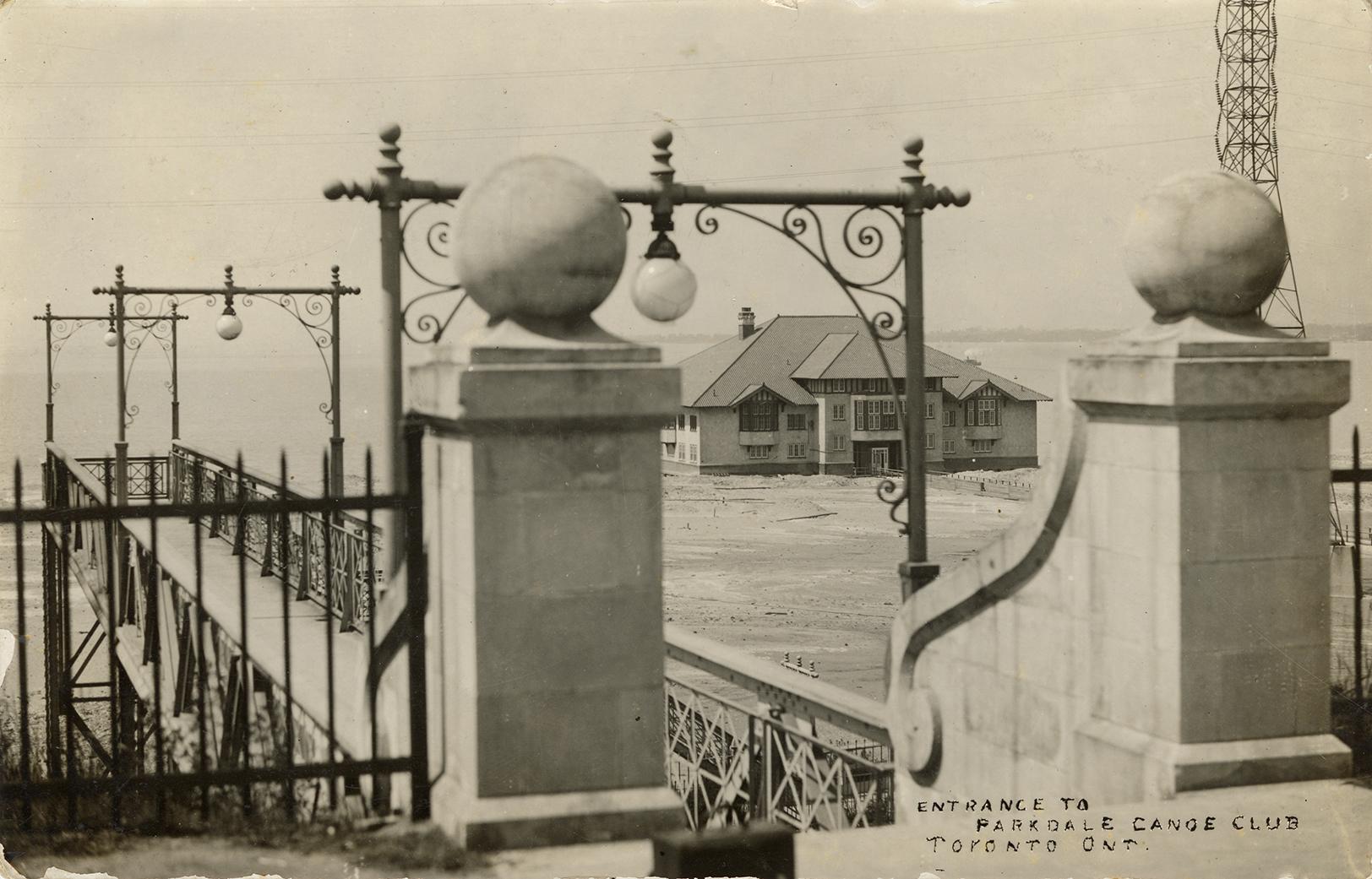 Black and white photograph of a large building on the other side of a stone gate.