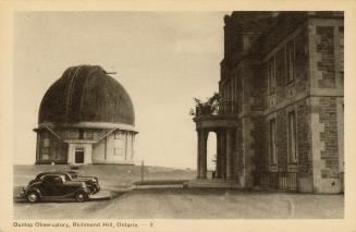 Black and white photograph of two cars parked outside a stone building. Domed building in the b ...