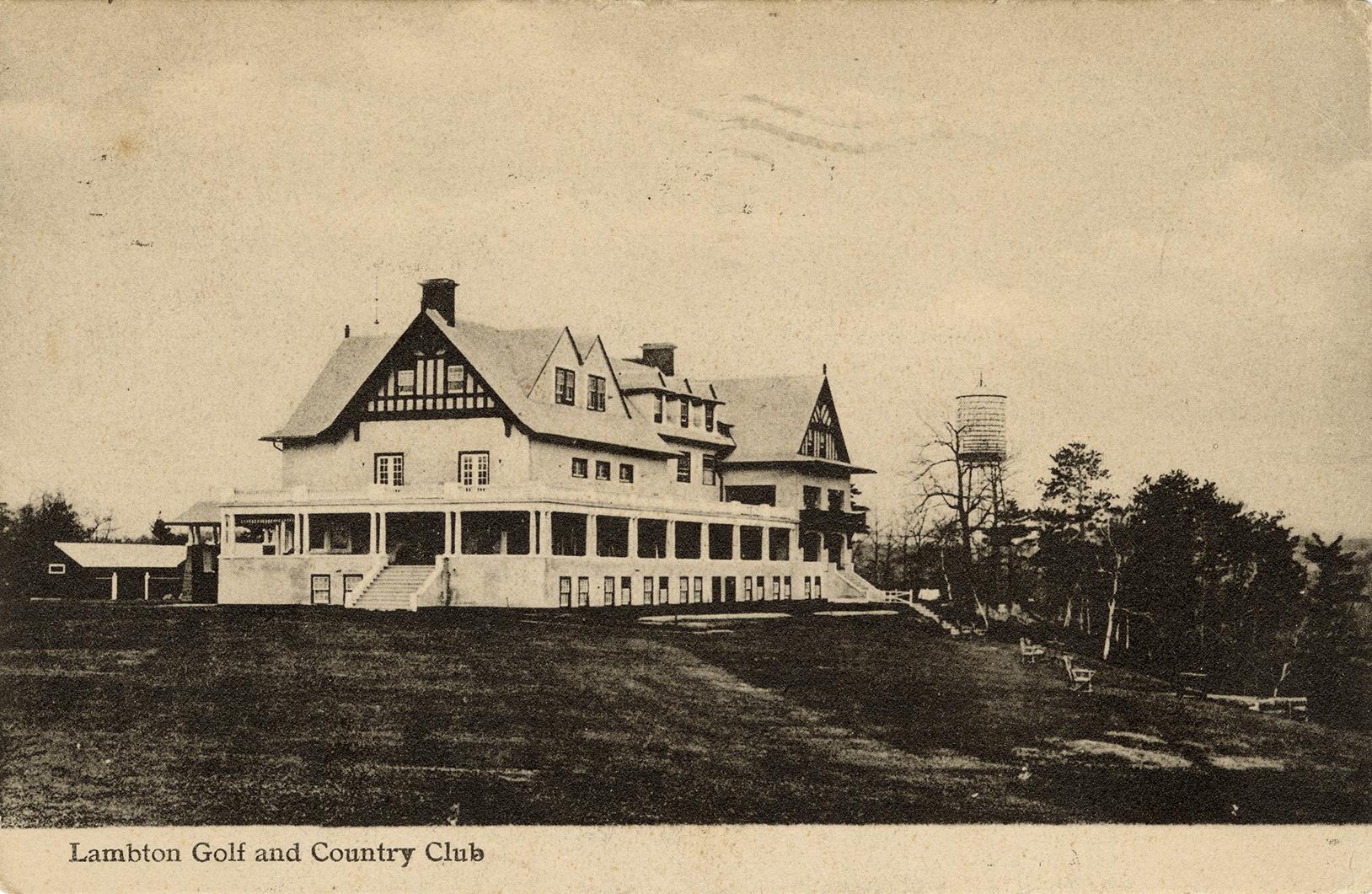 Black and white photograph of a large house with a wrap around veranda.