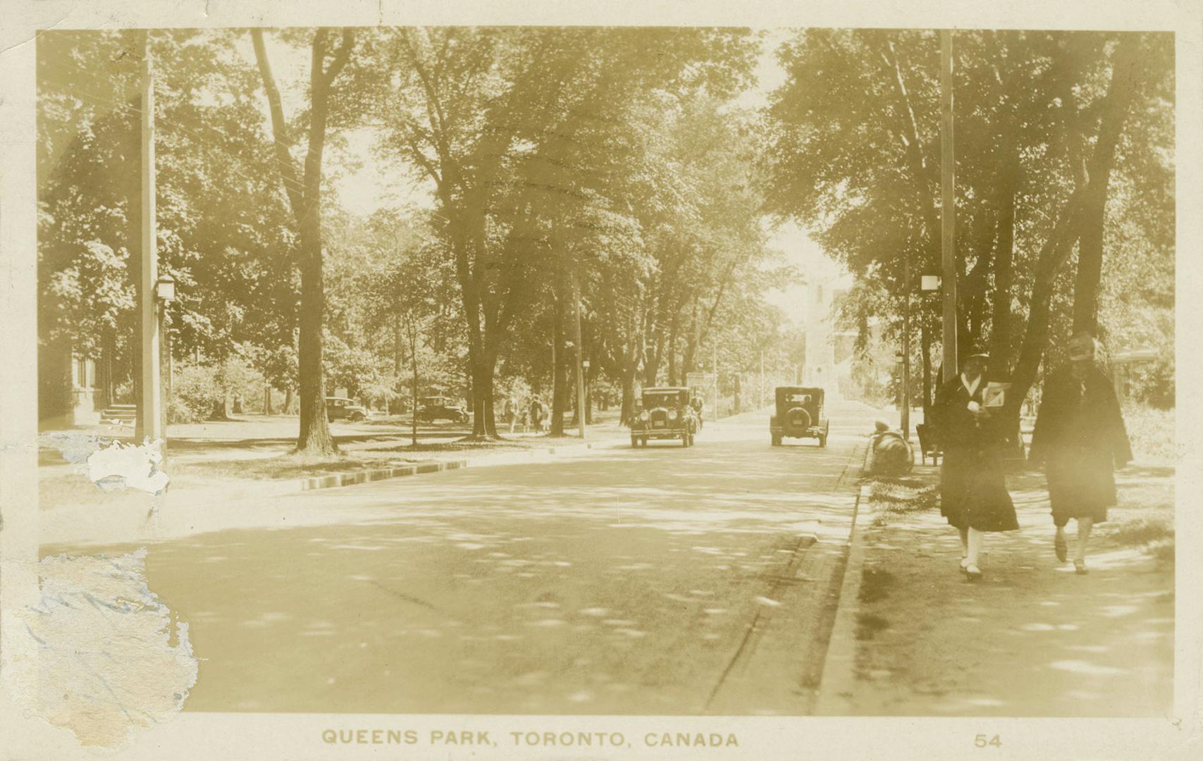 Sepia toned photograph of automobiles on a road running through a wooded area.