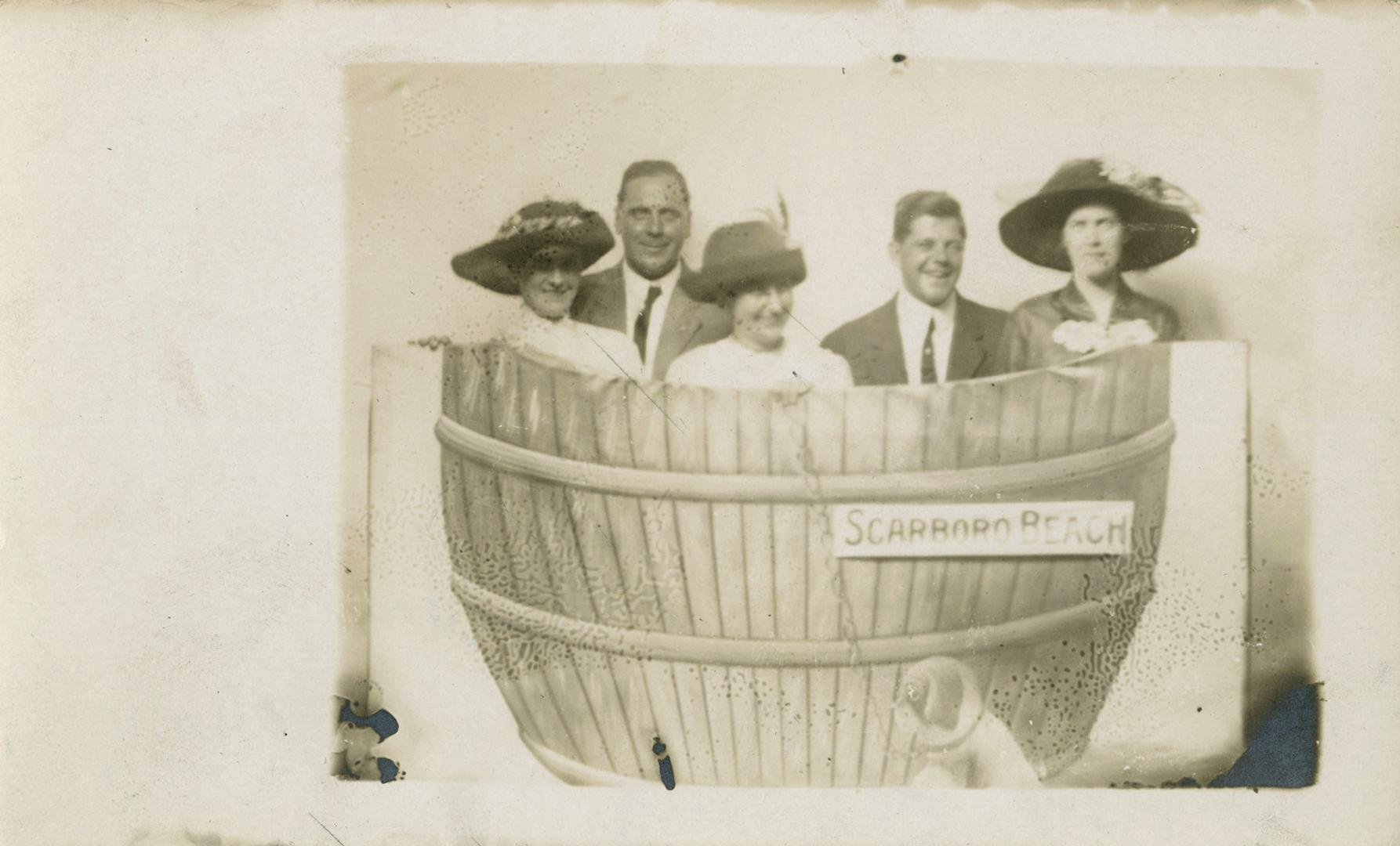 Black and white photograph of three ladies and two men posing for a photograph on a faux barrel ...