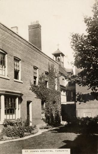 Black and white photo postcard depicting the exterior side wall of a hospital with a chimney an ...