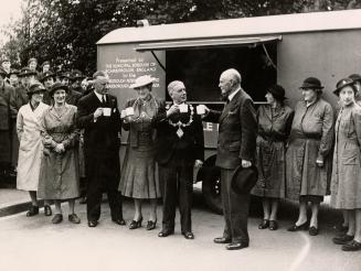 Picture of officials and other people standing in front of a canteen truck. 