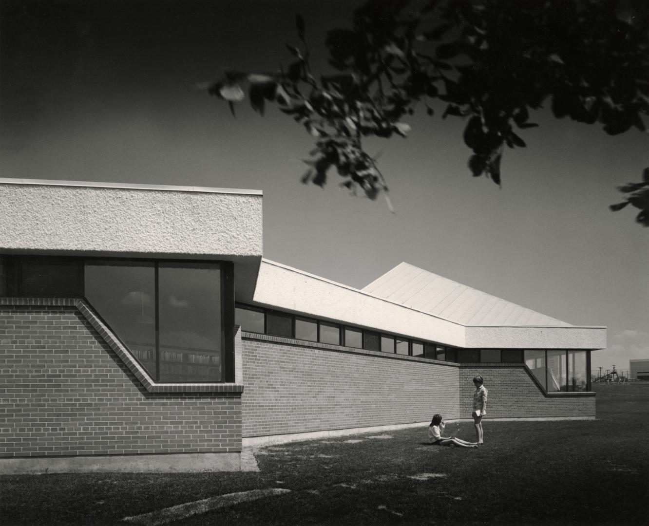 Picture of one storey library building and two people on lawn. 