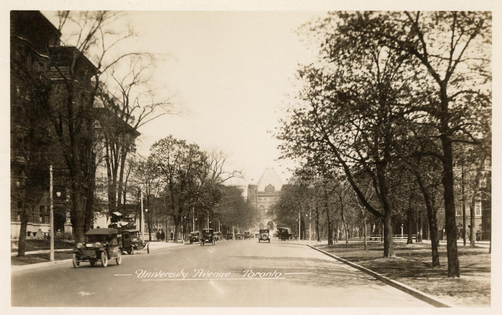 Black and white photograph of a wide, city street with trees on either side and down the median ...