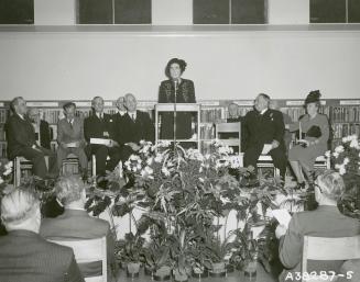 Picture of a woman speaking at a microphone and other people seated on both sides of her. 