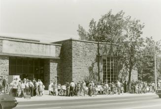 Picture of a crowd of people browsing tables outside a library building. 