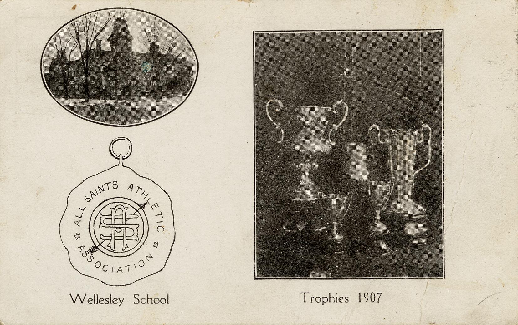 Black and white photograph of a large collegiate building. Five trophies in the foreground.