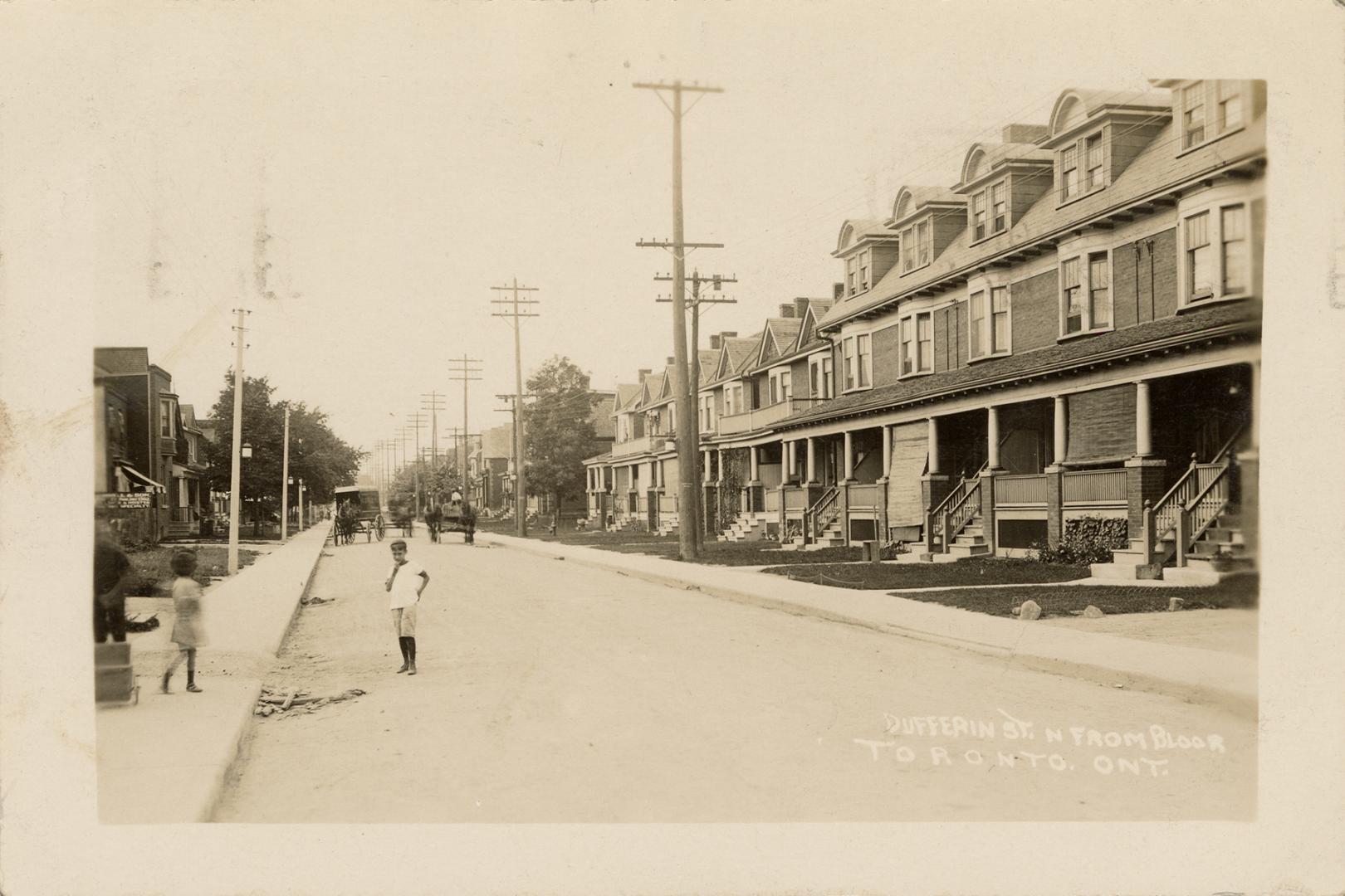 Black and white photograph of three story houses lining a city street.