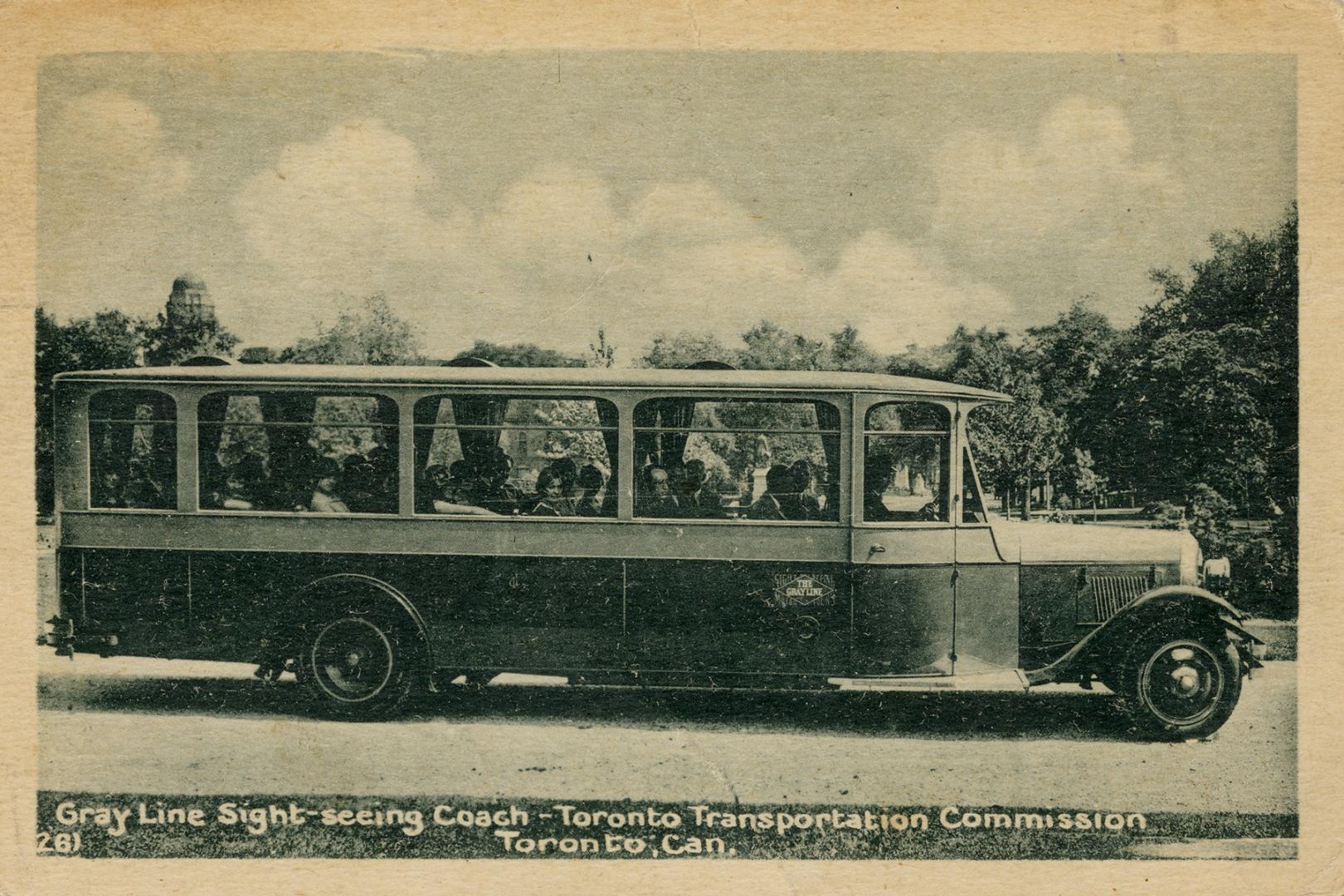 Black and white photograph of long bus coach with passengers inside.