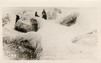 Black and white photograph of a frozen beach shoreline with people standing amidst the ice.