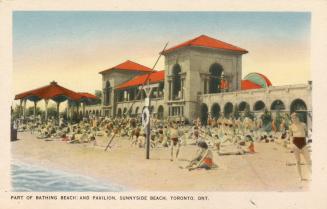 Colorized photograph of many people sitting on a beach in front of building with a long set of  ...