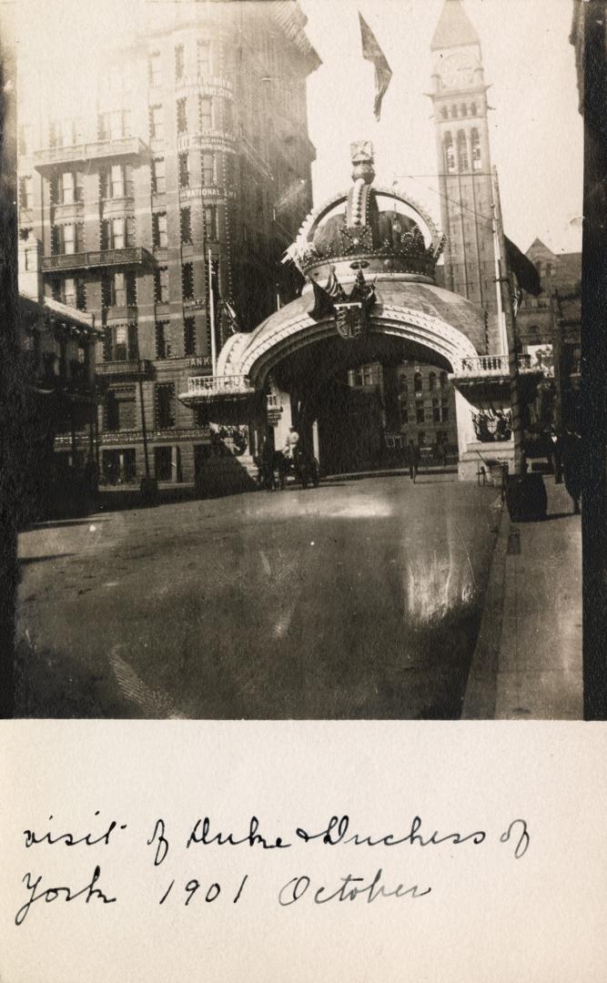 Black and white photograph of an arch with a gigantic crown on the top of it spanning a city st ...