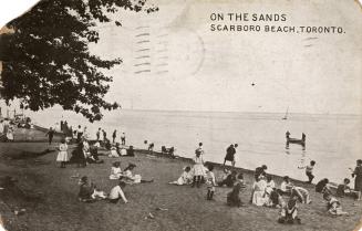 Black and white photograph of many people sitting on a beach watching people in boats and canoe ...