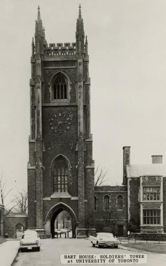 Black and white photograph of a bell and clock tower with a gothic archway providing access thr ...