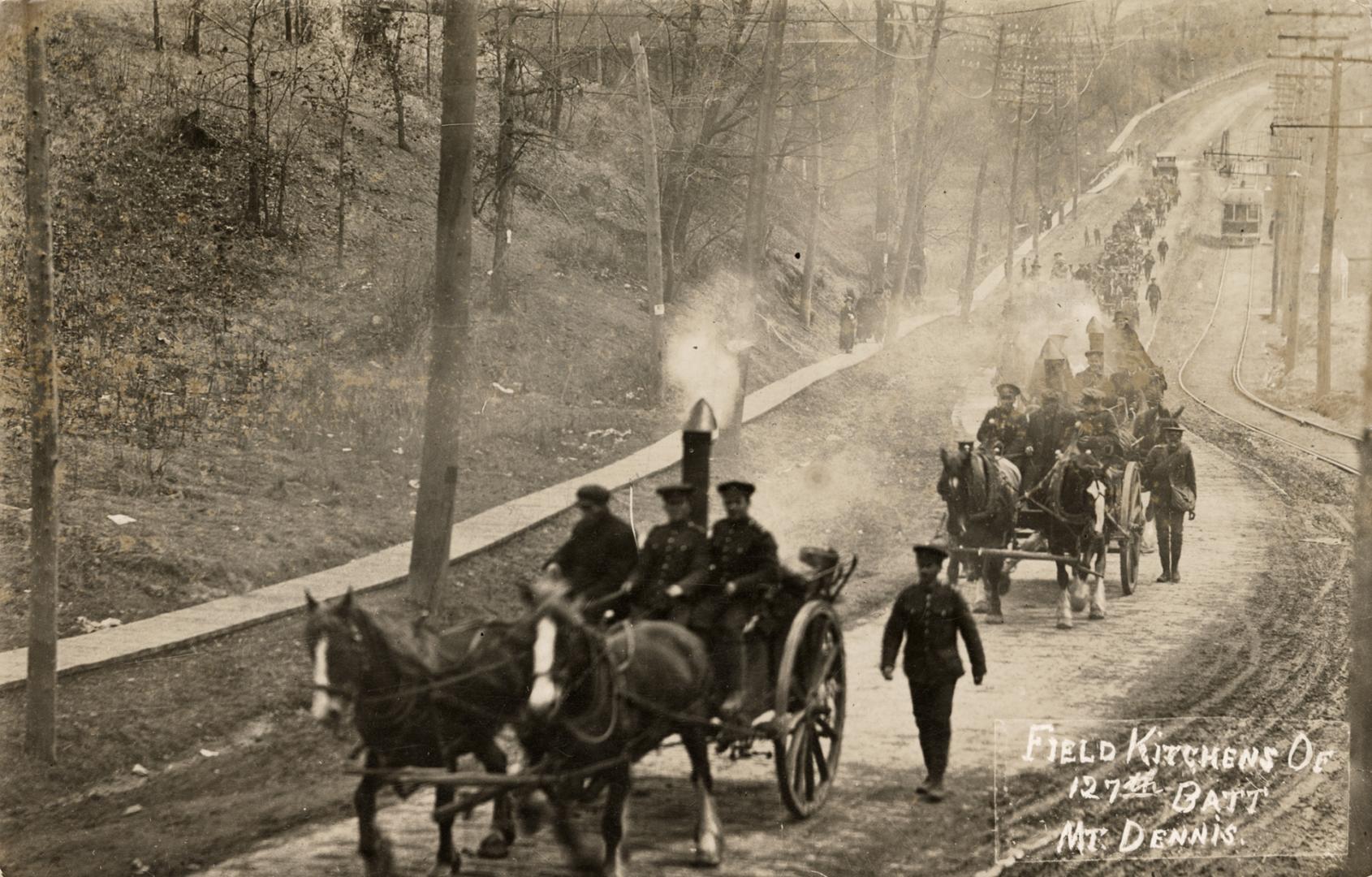 Black and white photograph of soldiers and horse carts walking along a paved road.