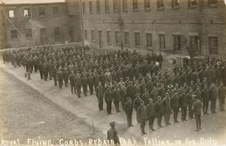 Black and white photograph of soldiers in uniform standing in lines in quadrangle.