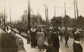 Black and white photograph of soldiers in uniform marching along a street with civilians lookin ...