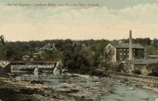 Colorized photograph of a river running under a bridge beside a square, stone building.