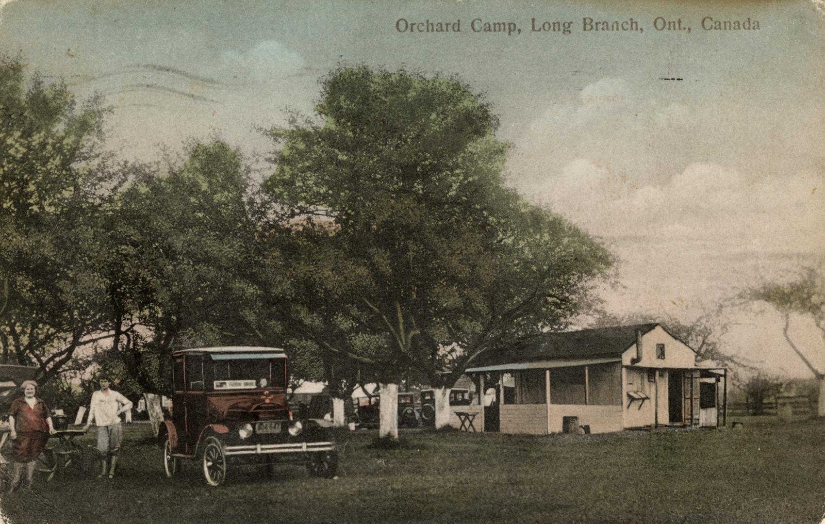 Colorized photograph of two women standing beside a car in front of a frame summer home.