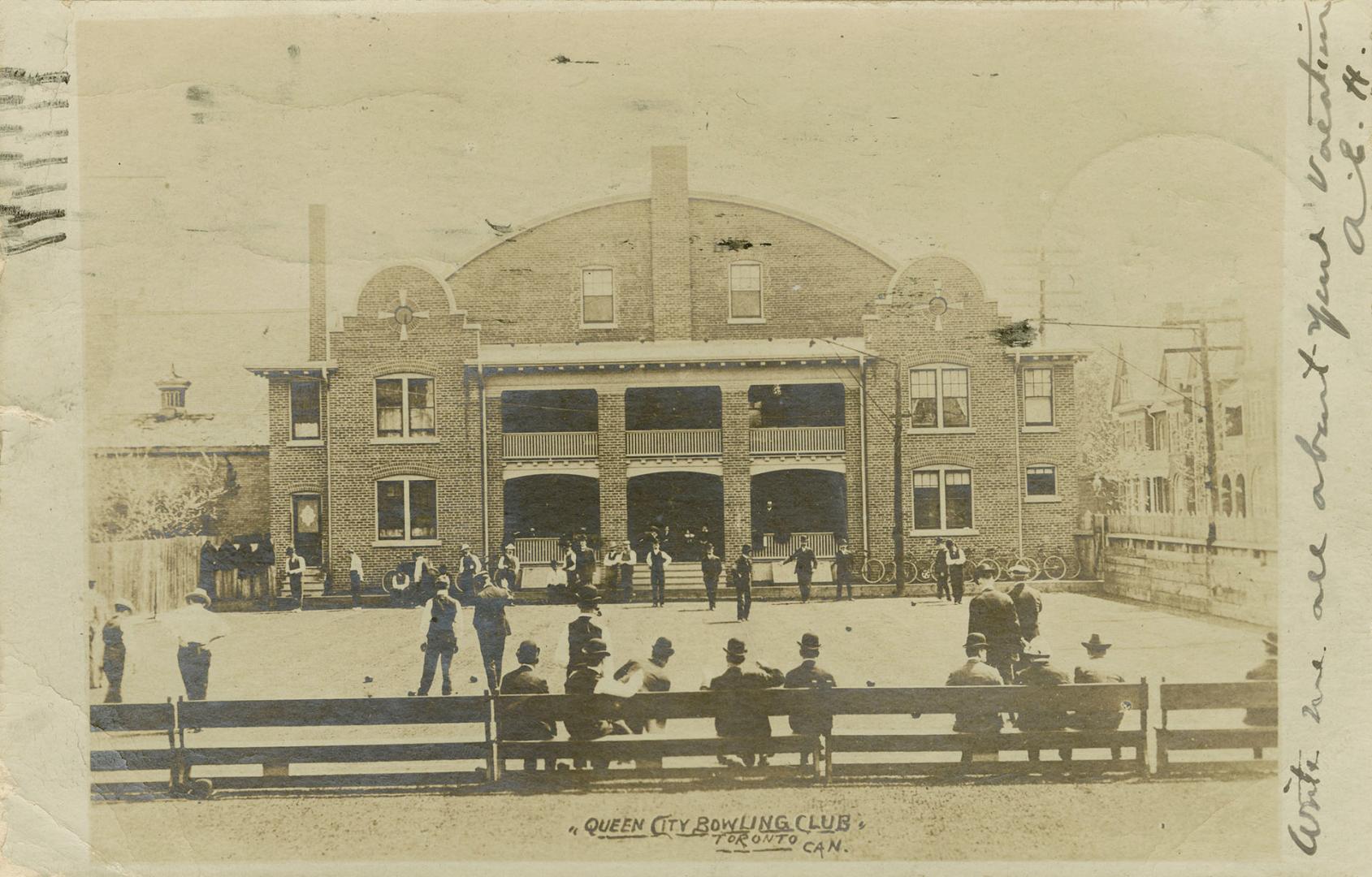 Black and white photograph of a three story brick building with balconies in the middle.