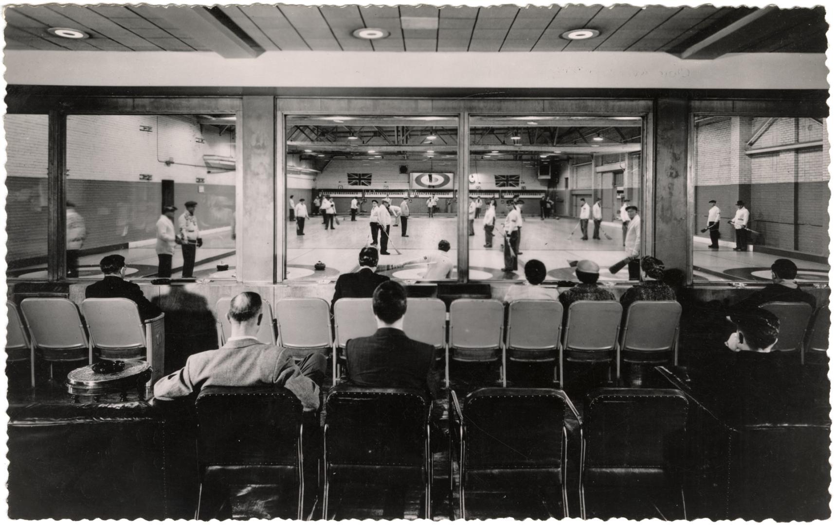 Black and white photo postcard depicting a room of men engaged in curling while onlookers watch ...