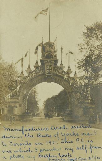 Black and white photograph of a large stone arch spanning a paved road with people and carriage…