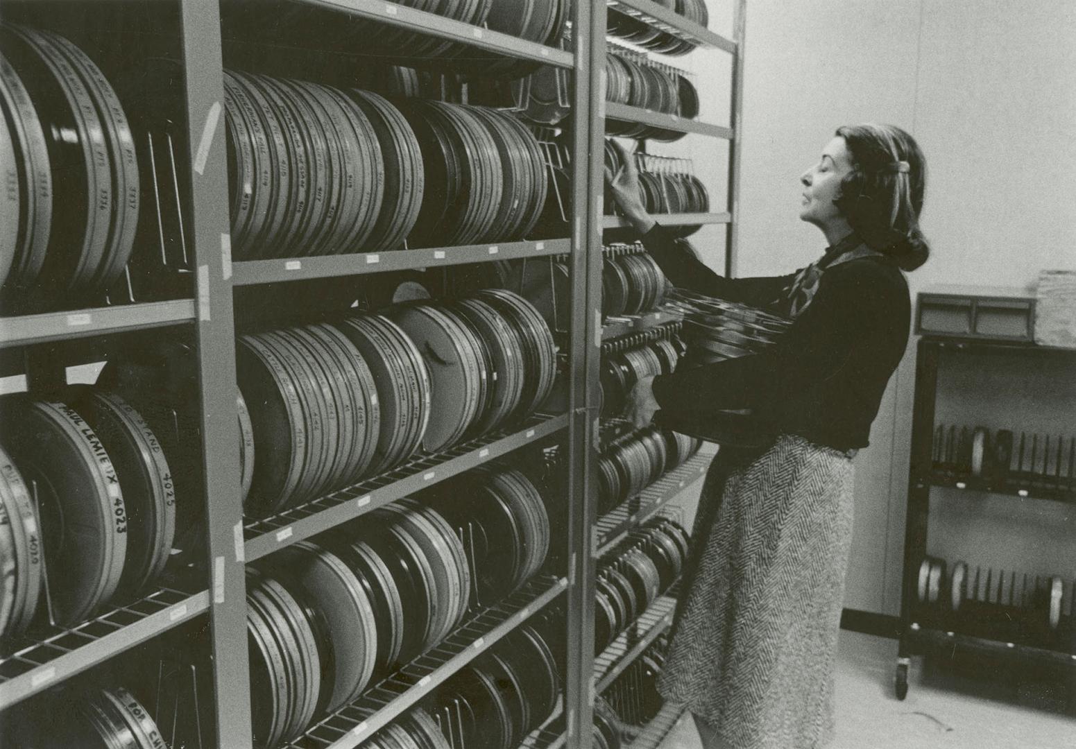 Picture of a woman shelving films on a large shelf full of films. 