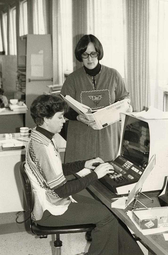 Picture of two librarians at a computer cataloguing machine. 