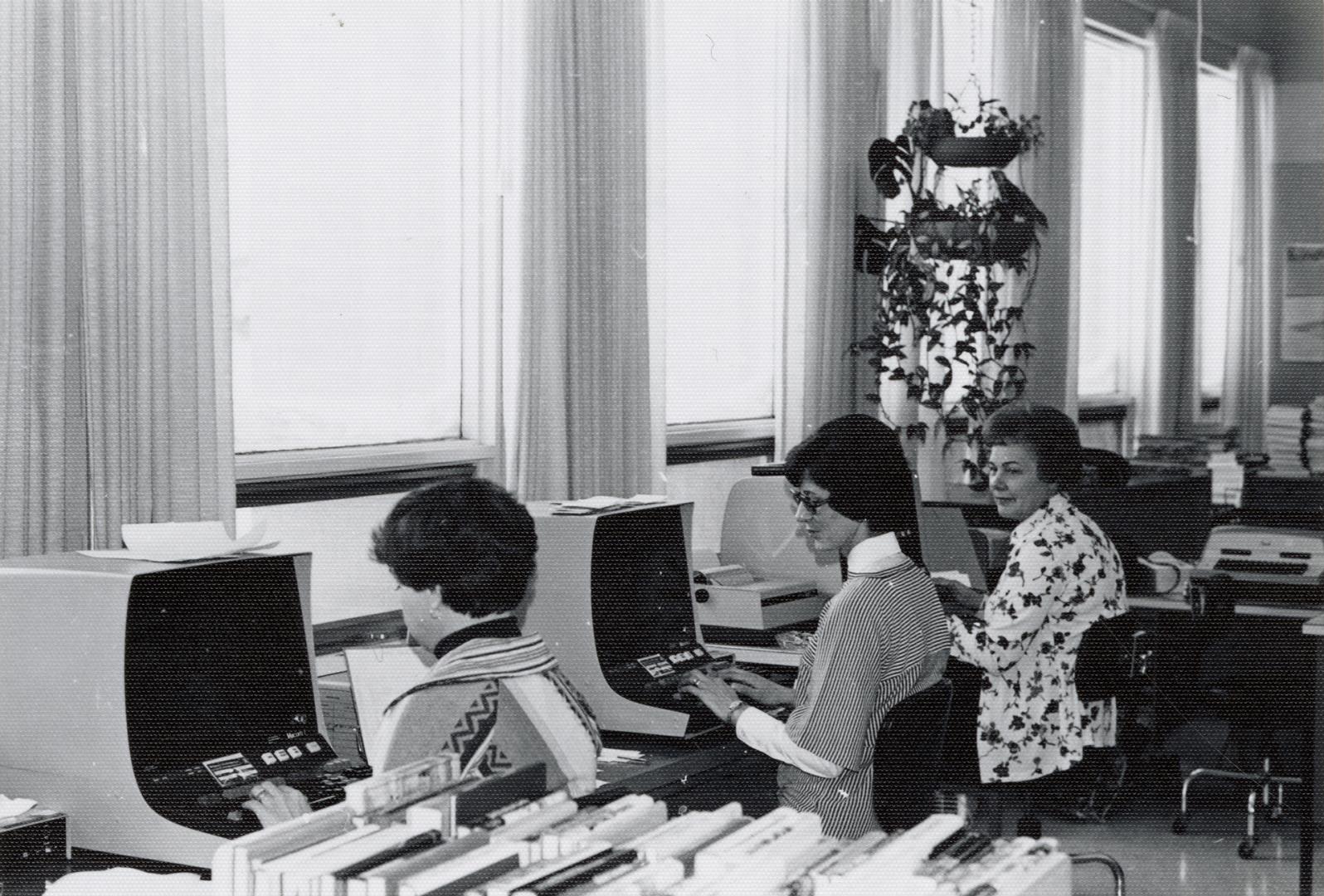 Picture of three librarians at a computer cataloguing machine. 