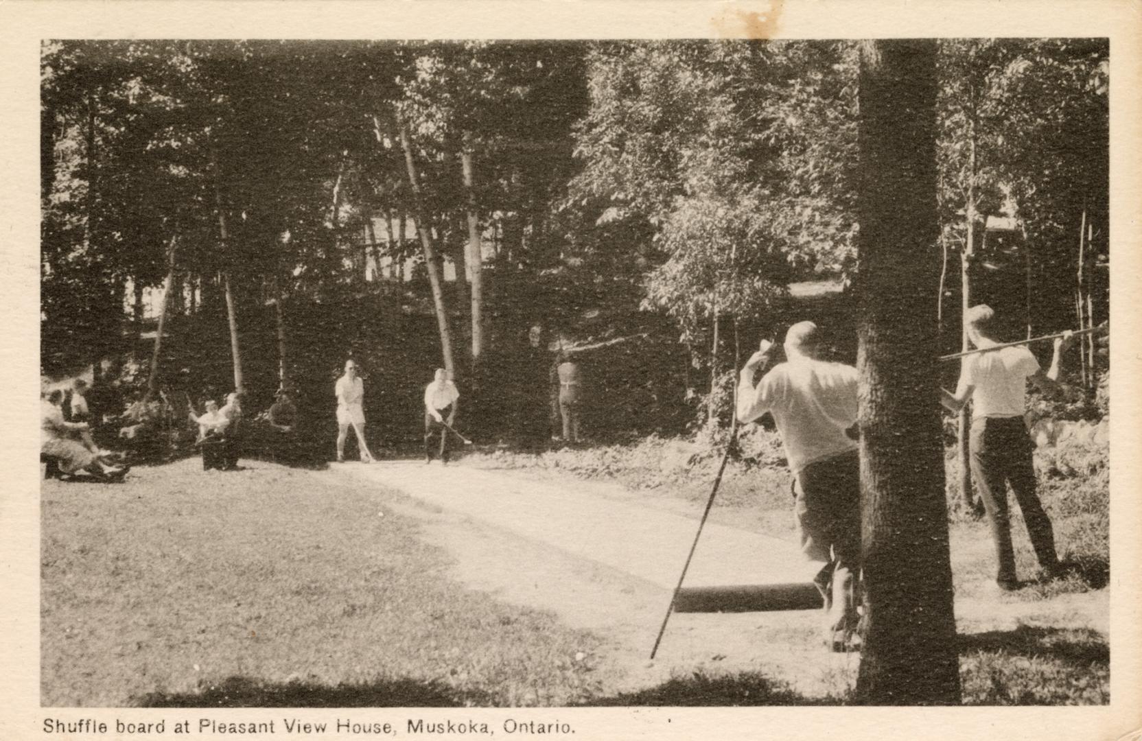 Black and white photograph of a four people playing shuffle board, surrounded by trees.