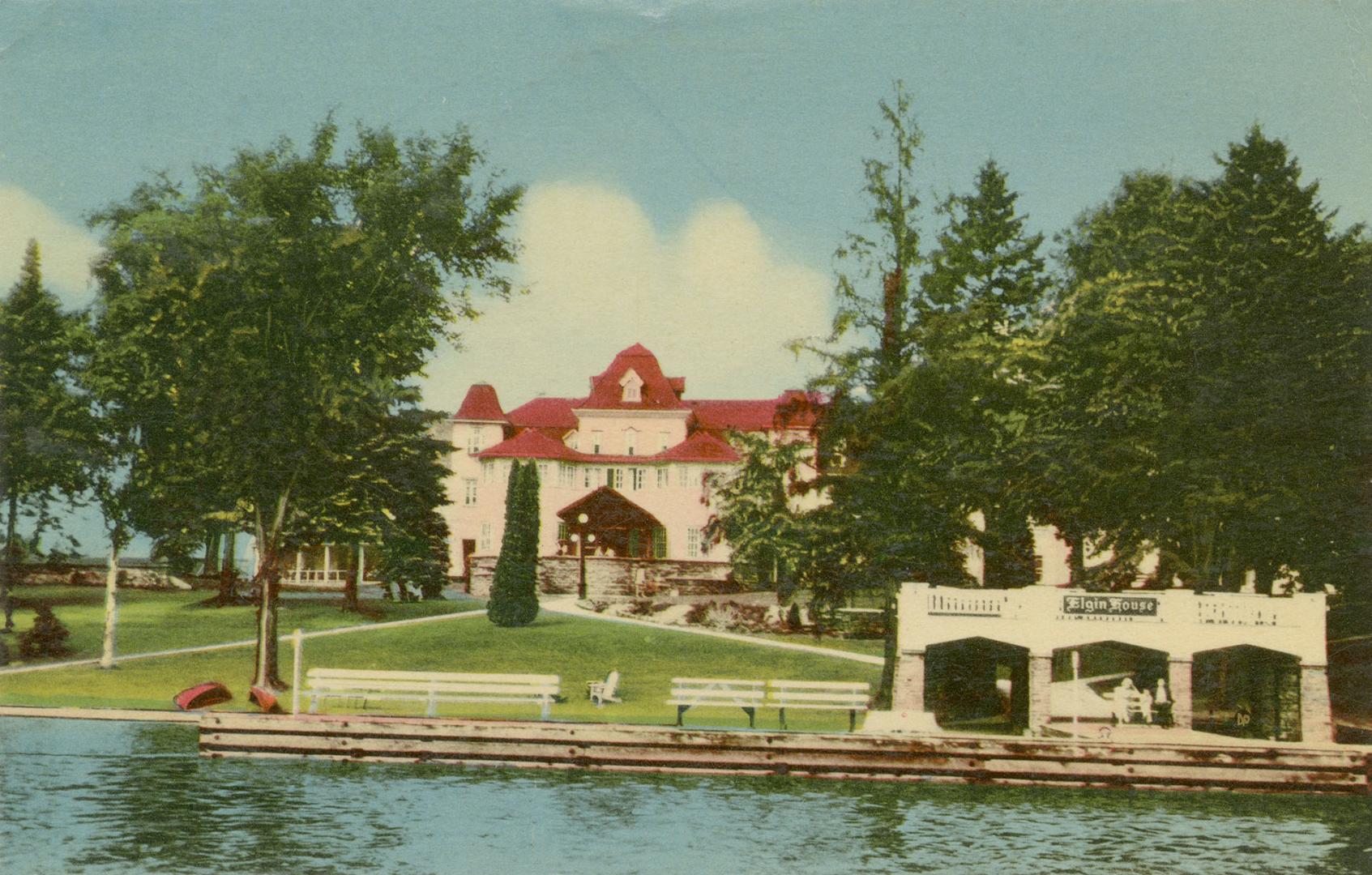 Colorized photograph of a large resort building on the edge of a smooth waterway.