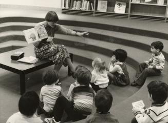 Picture of a librarian telling a story to children seated on floor. 