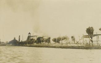 Black and white photograph of a long stretch of a bridge leading to an amusement park.