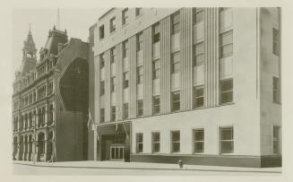 Black and white photo postcard depicting an 5-story concrete office building. The back of the c…