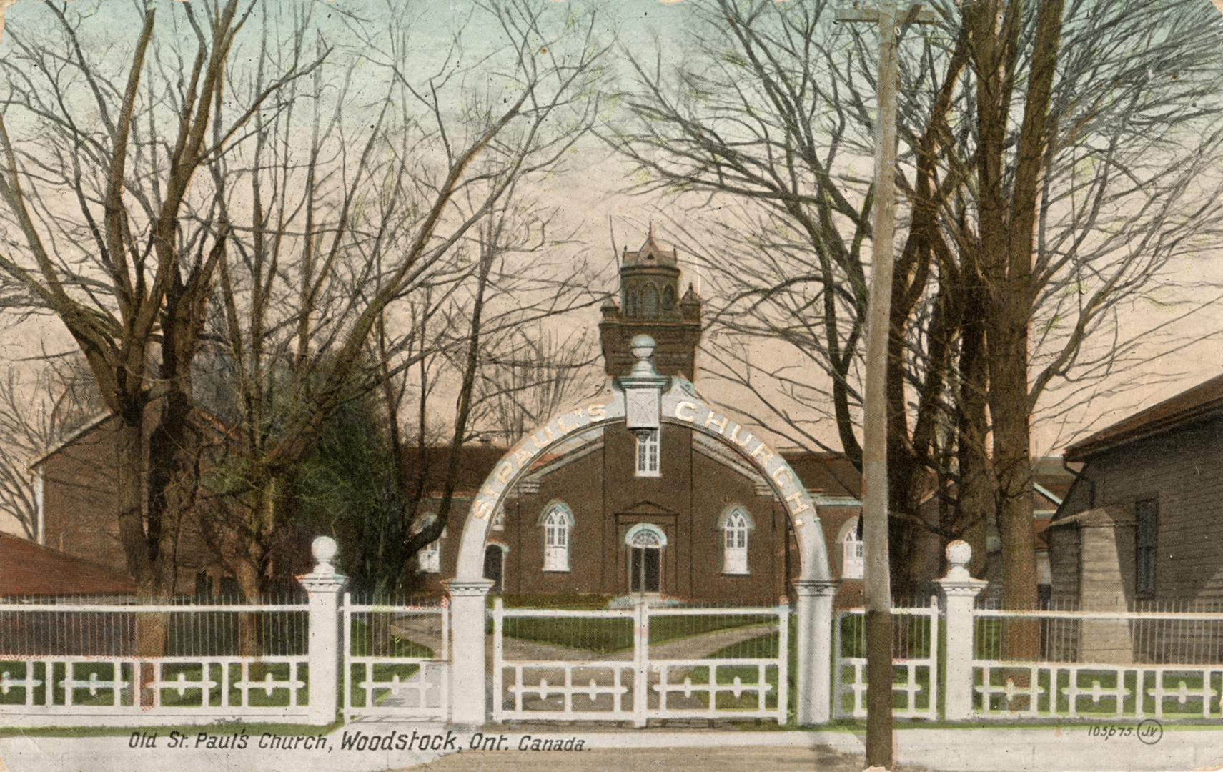 Colorized photograph of a red brick church behind a white fence.